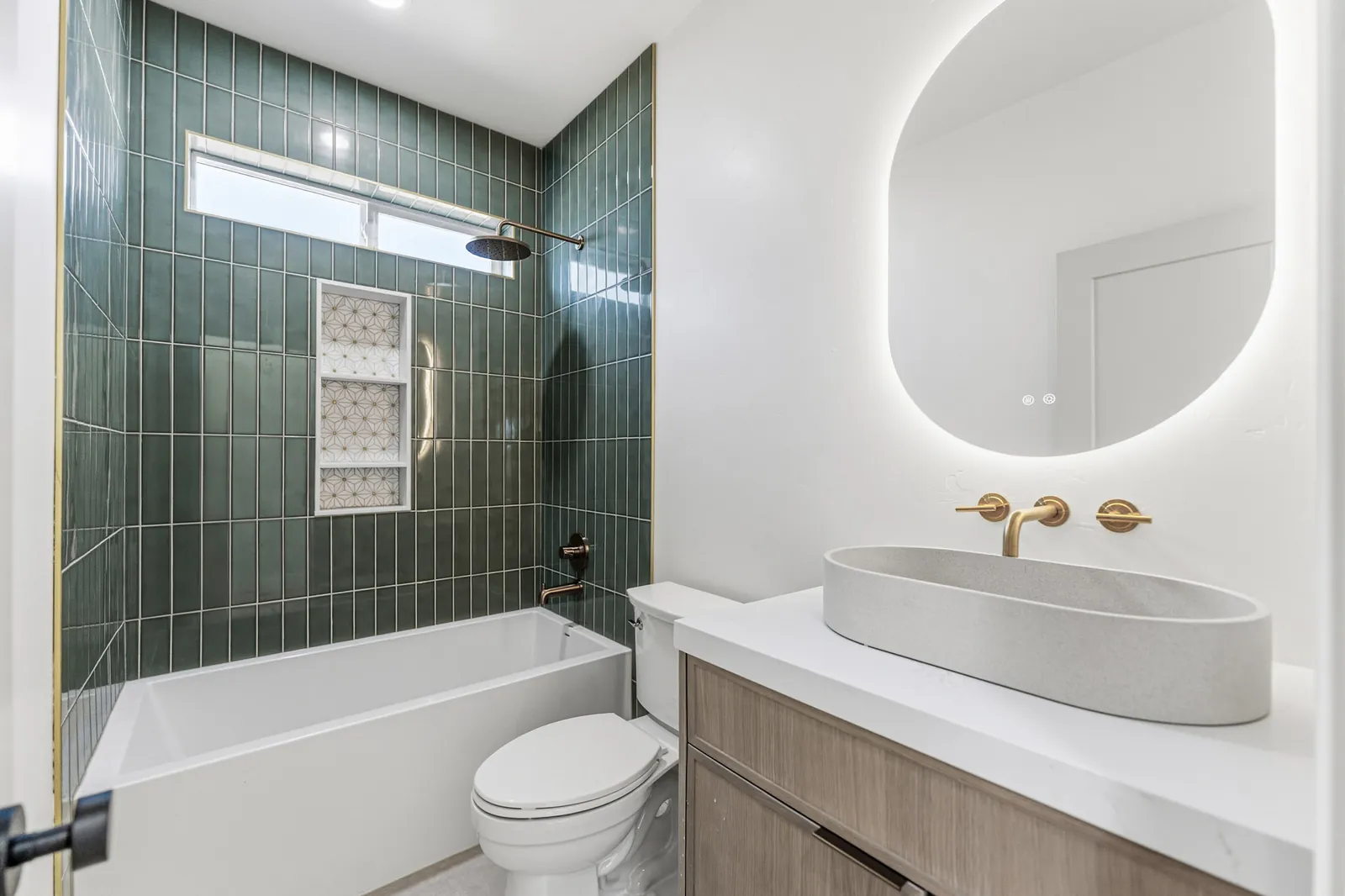 Bathtub and shower surround in green glazed tile beside a white oak vanity