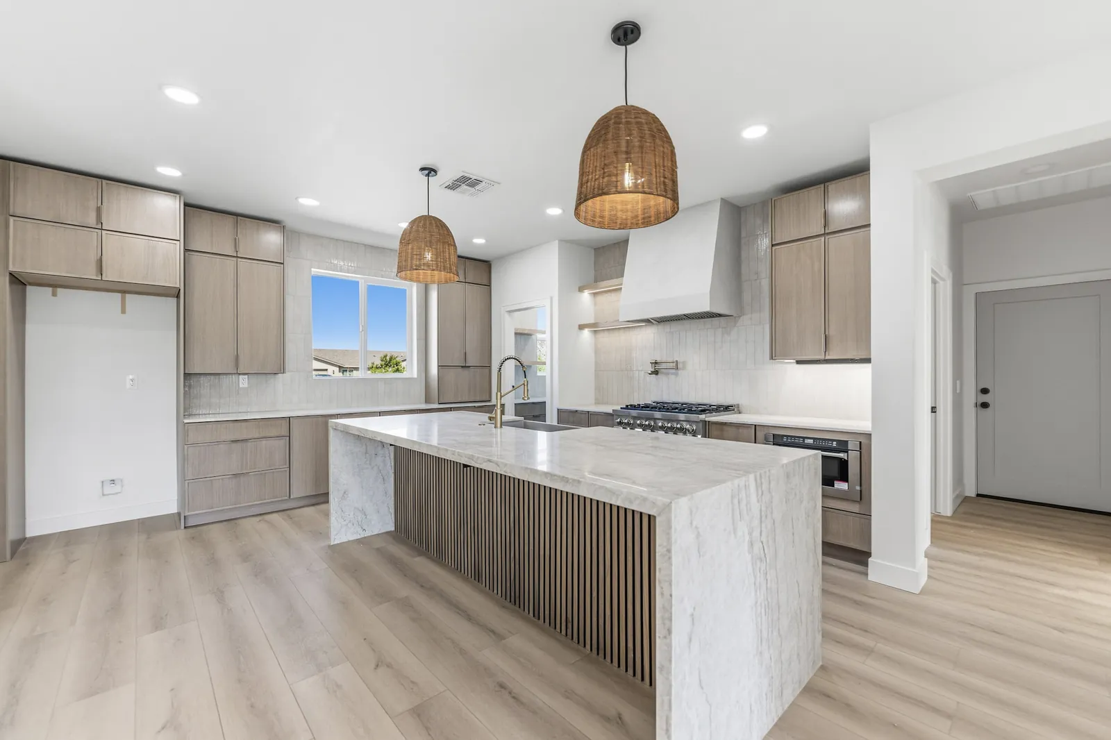 Kitchen island with a fluted white oak base, marble counter and woven pendant lights