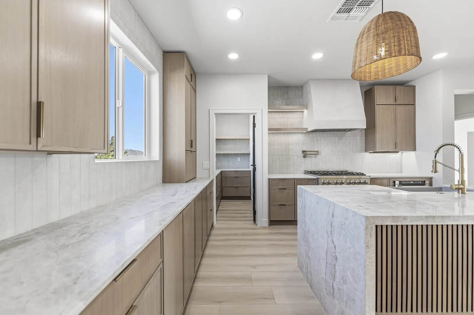 Kitchen counter run in marble with a brass bridge faucet and oak cabinets below