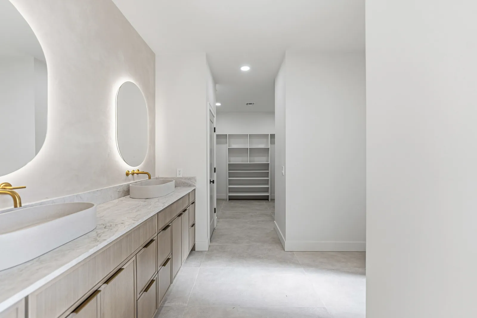 Primary bathroom double vanity with the walk-in closet shelving beyond