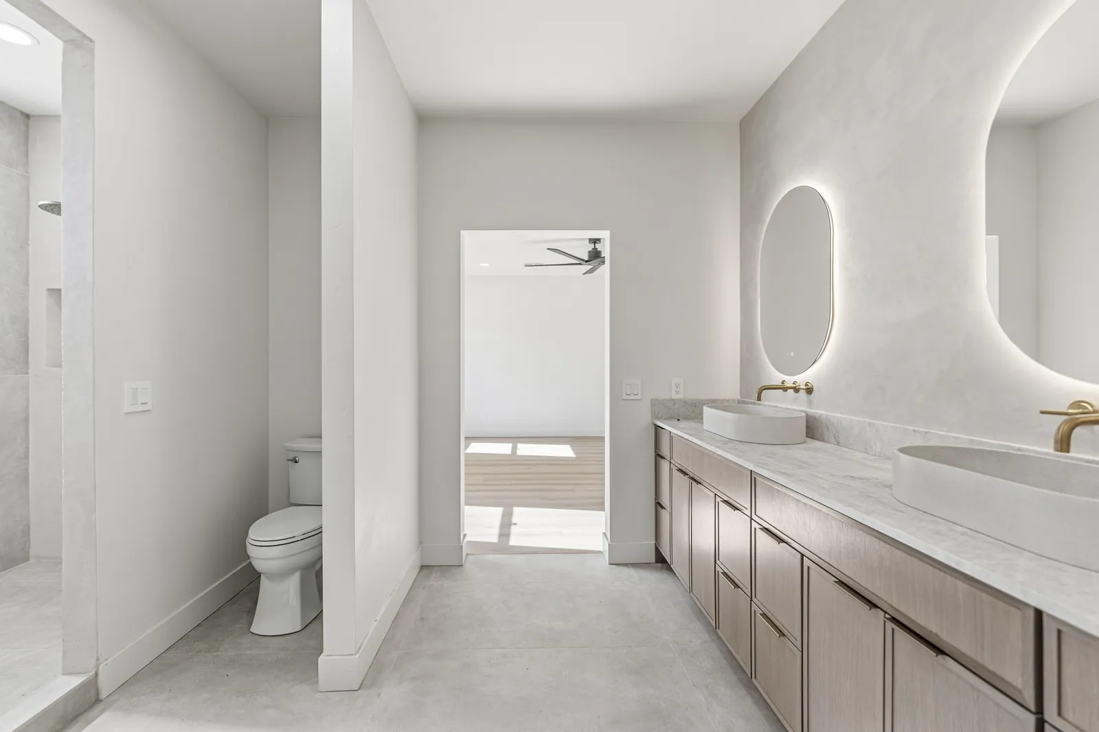 Bathroom vanity in white oak with a stone top and a backlit oval mirror