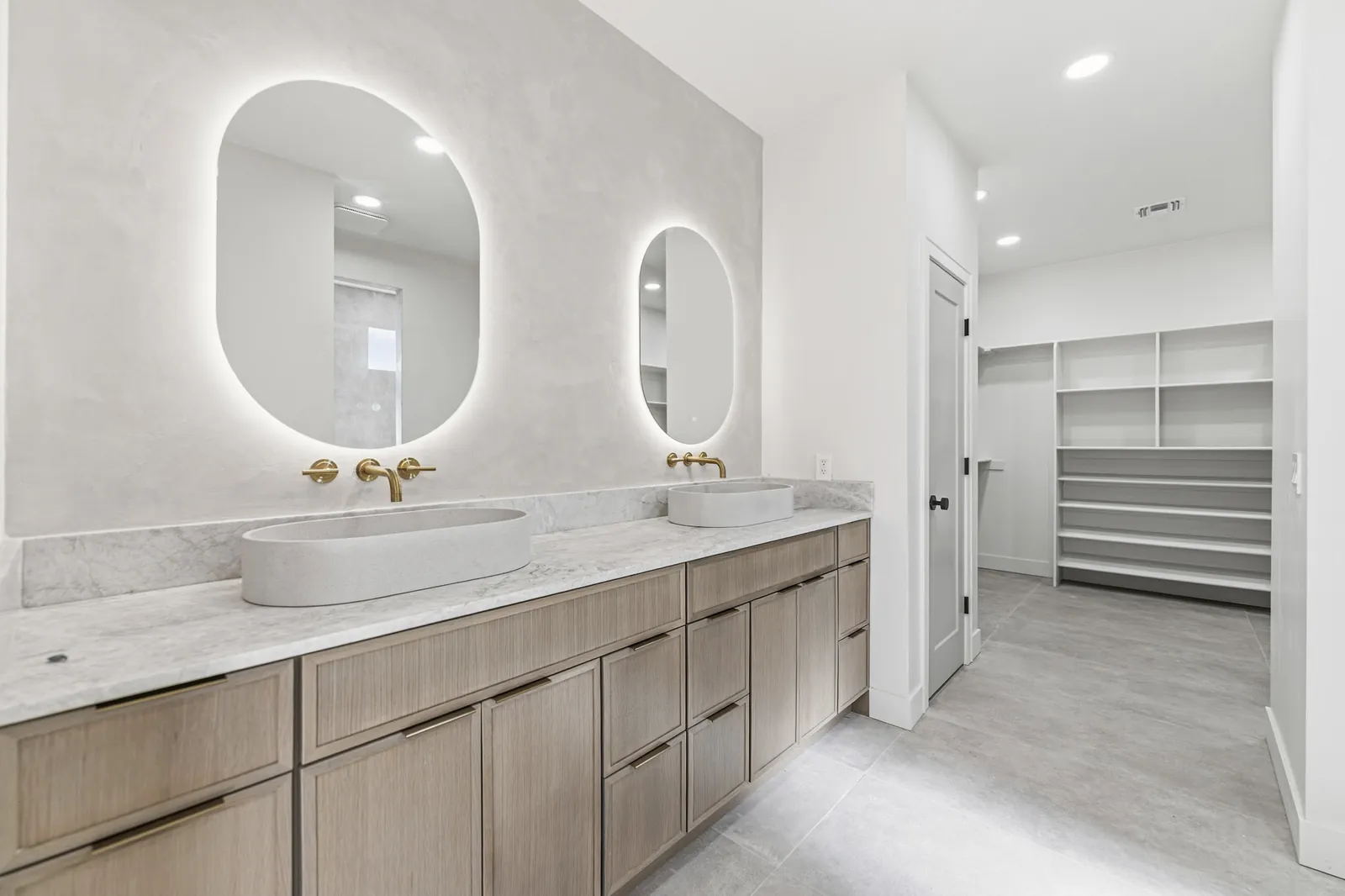 Primary bathroom with twin backlit oval mirrors above a marble double vanity