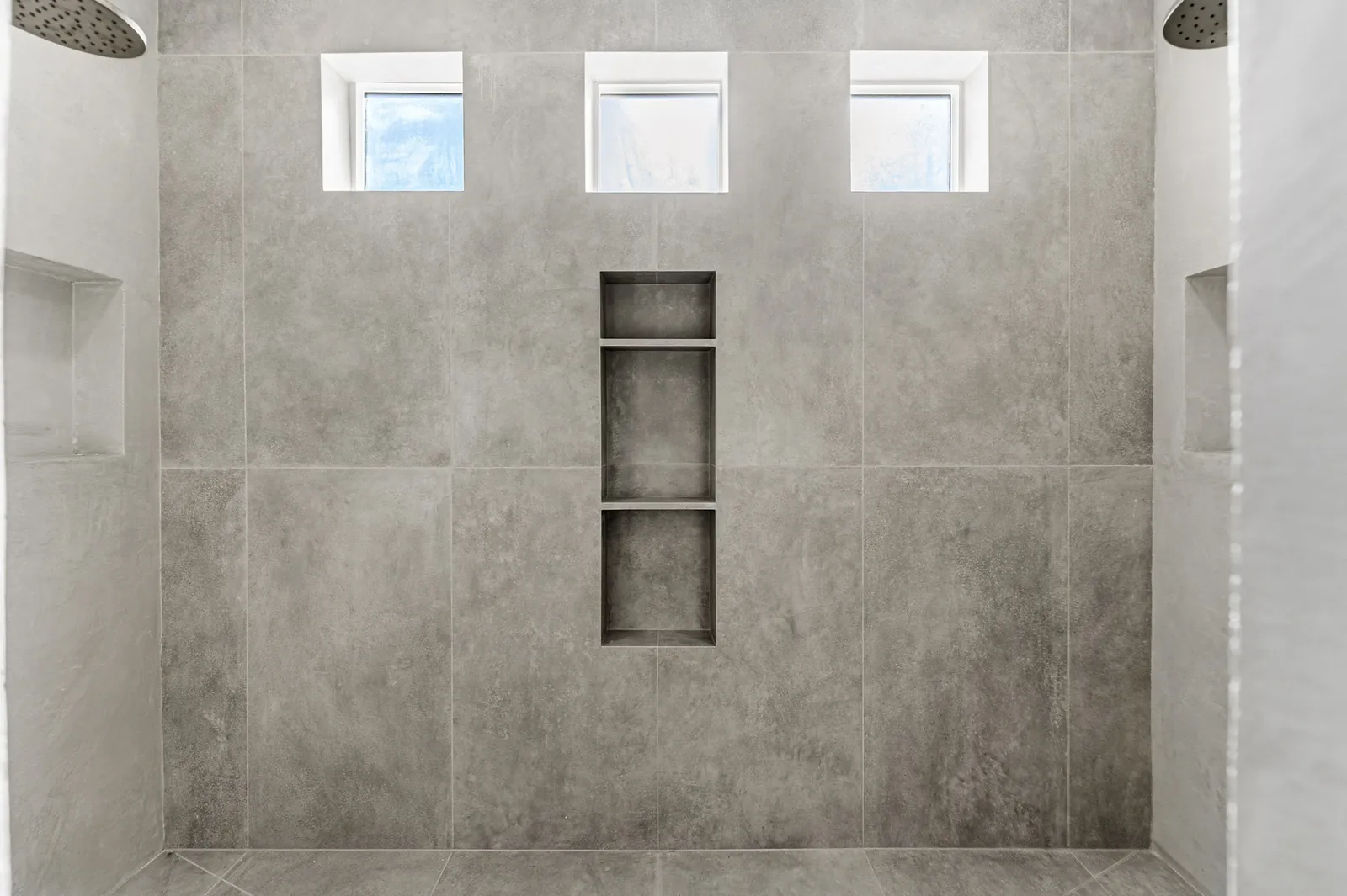 Walk-in shower tiled in large format stone with recessed niches and high windows