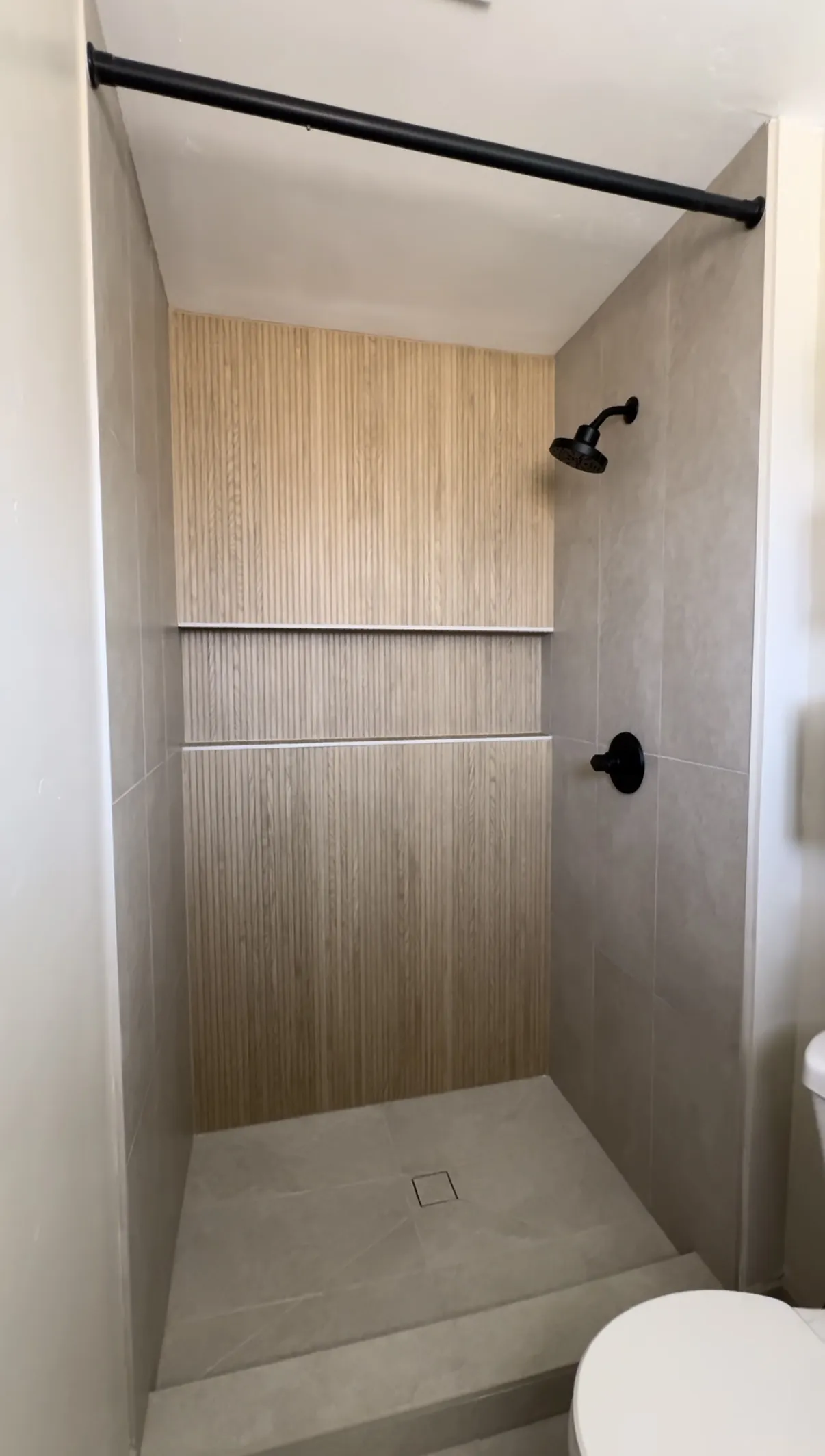 Walk-in shower lined in wood look tile with matte black fittings