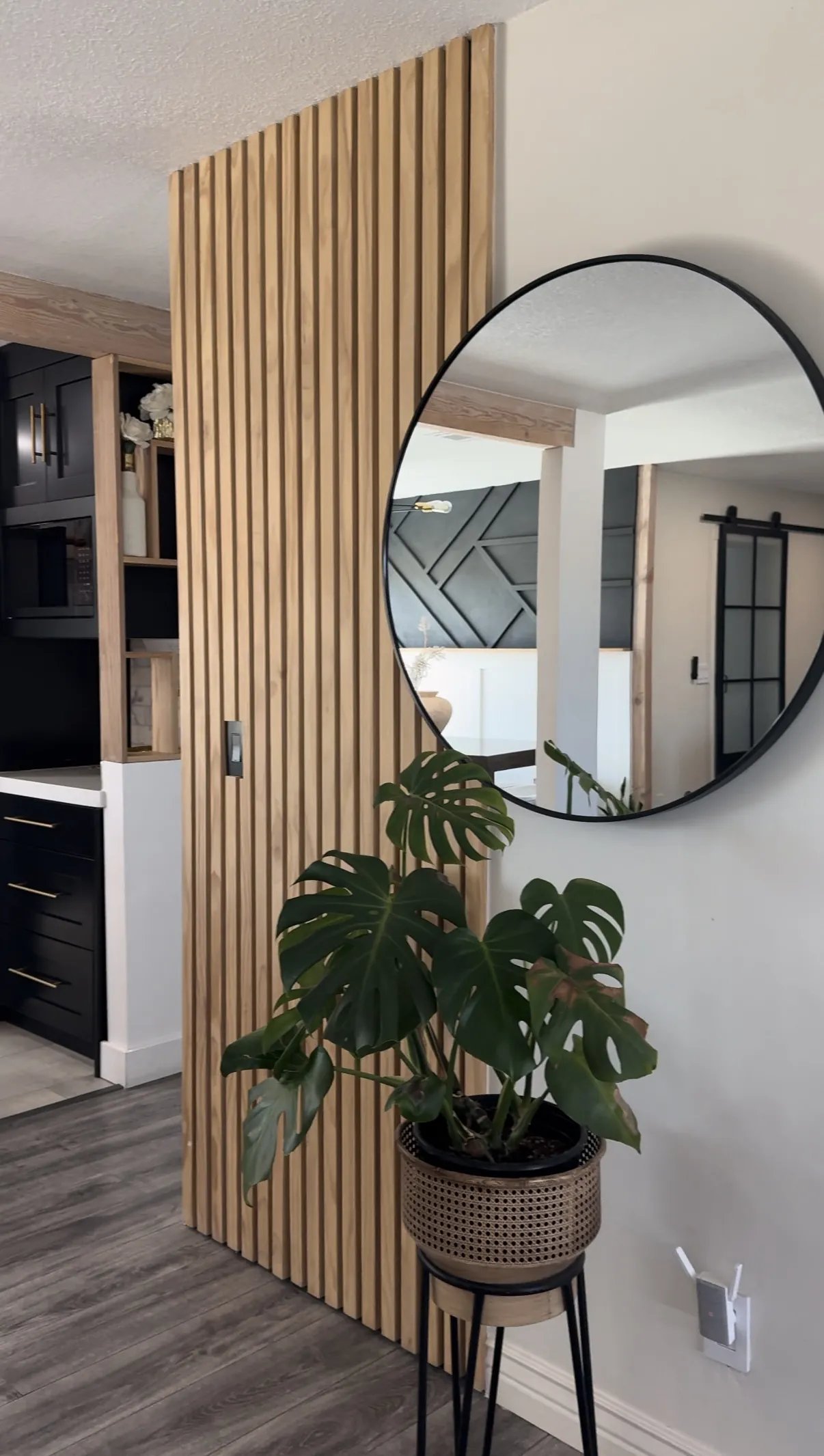 White oak slat divider between two rooms in a remodelled house, with a round mirror mounted on it